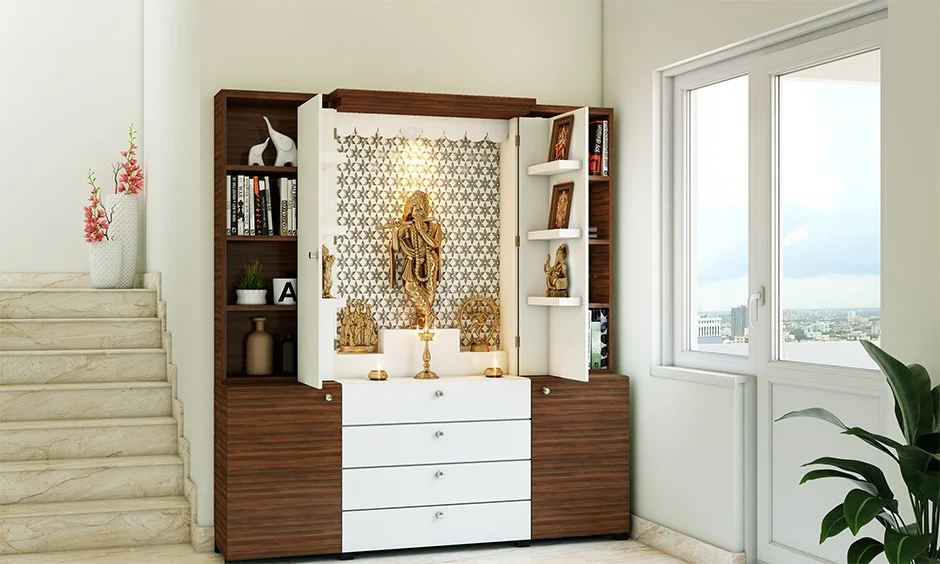 A walnut-finish mandir cabinet with white drawers opens to a star-pattern jaali backdrop and brass idols.