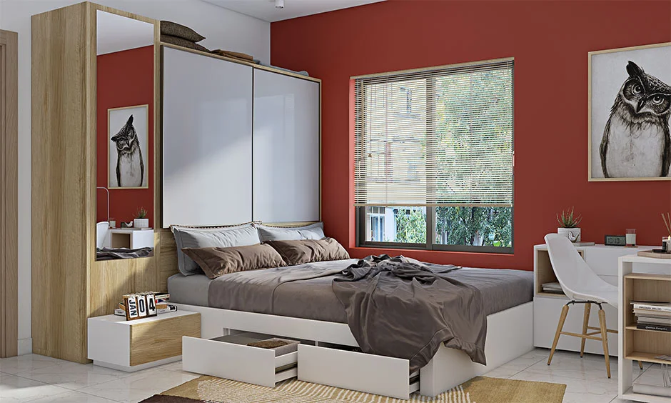 Bedroom interior with sunmica finish wardrobe and wooden storage bed against a red accent wall.