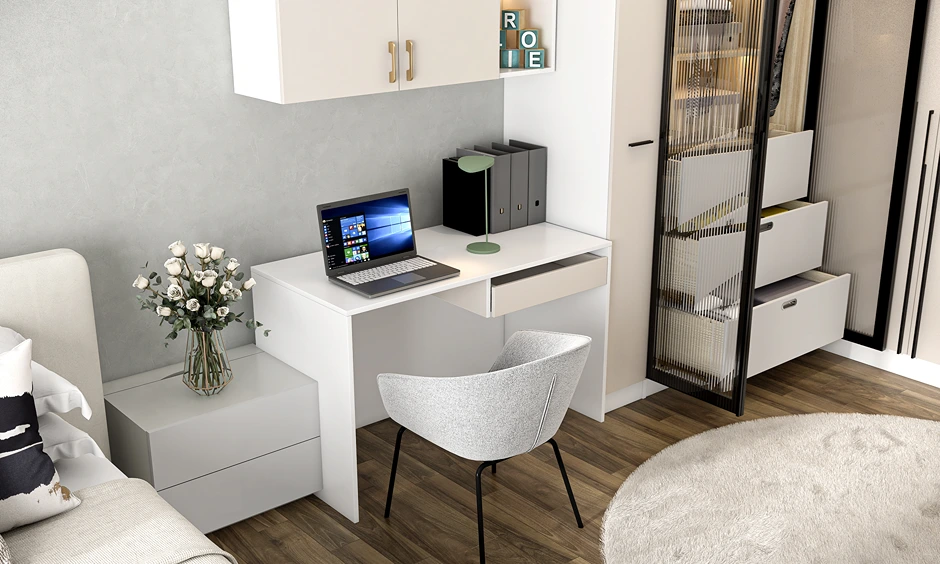 Modern white study desk with a laptop, green lamp, and overhead cabinets positioned next to a fluted glass wardrobe.
