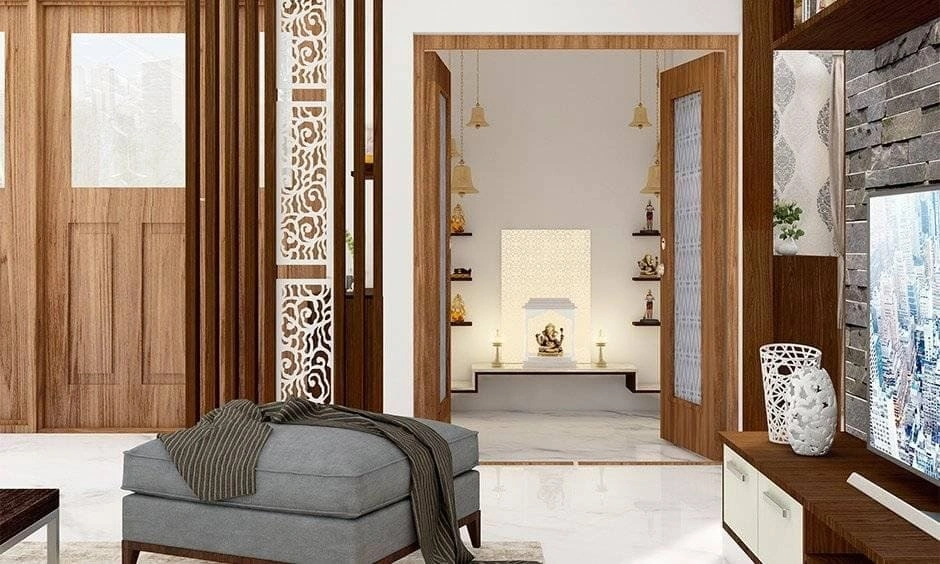 A white marble pooja room with storage drawers, hanging temple bells, and wooden jaali shutter doors.