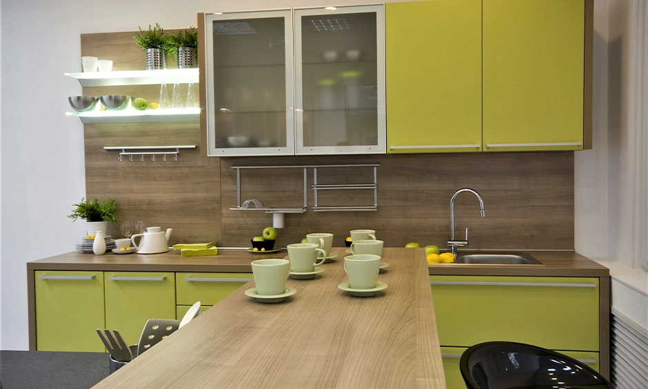 A modern kitchen combines green laminate base cabinets with light wood and glass-finish upper cabinets.